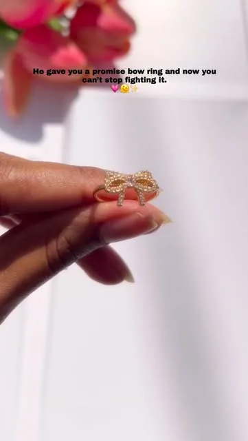 Gold bow promise ring held between fingers